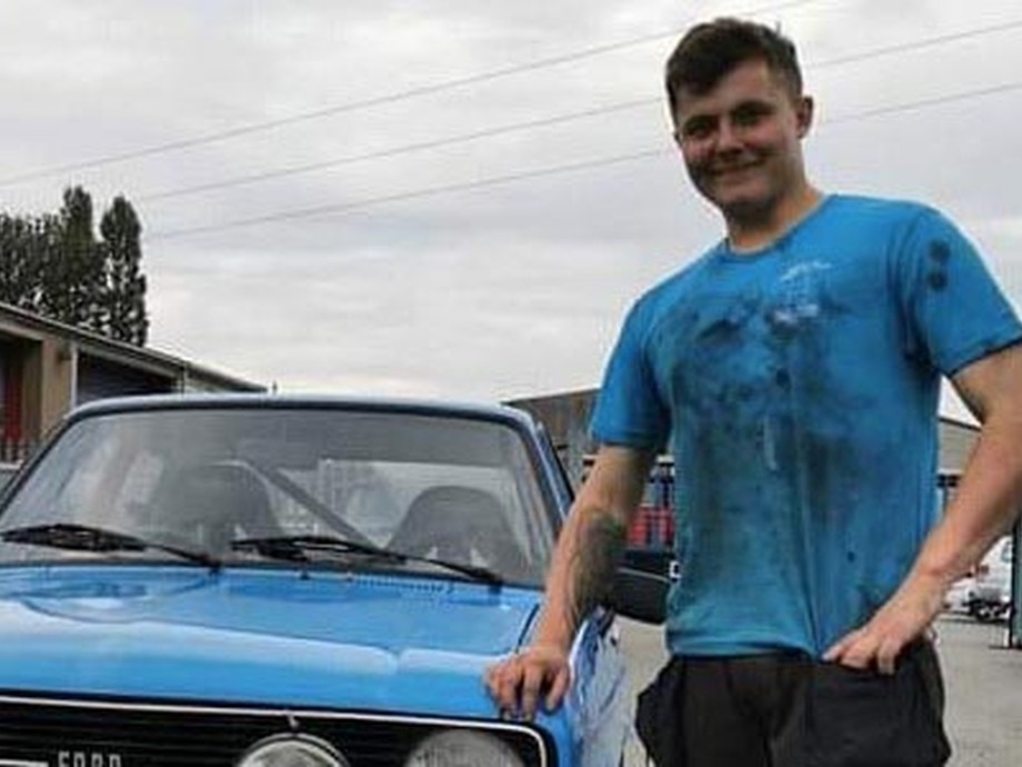 Tom standing in a blue t-shirt next to a car