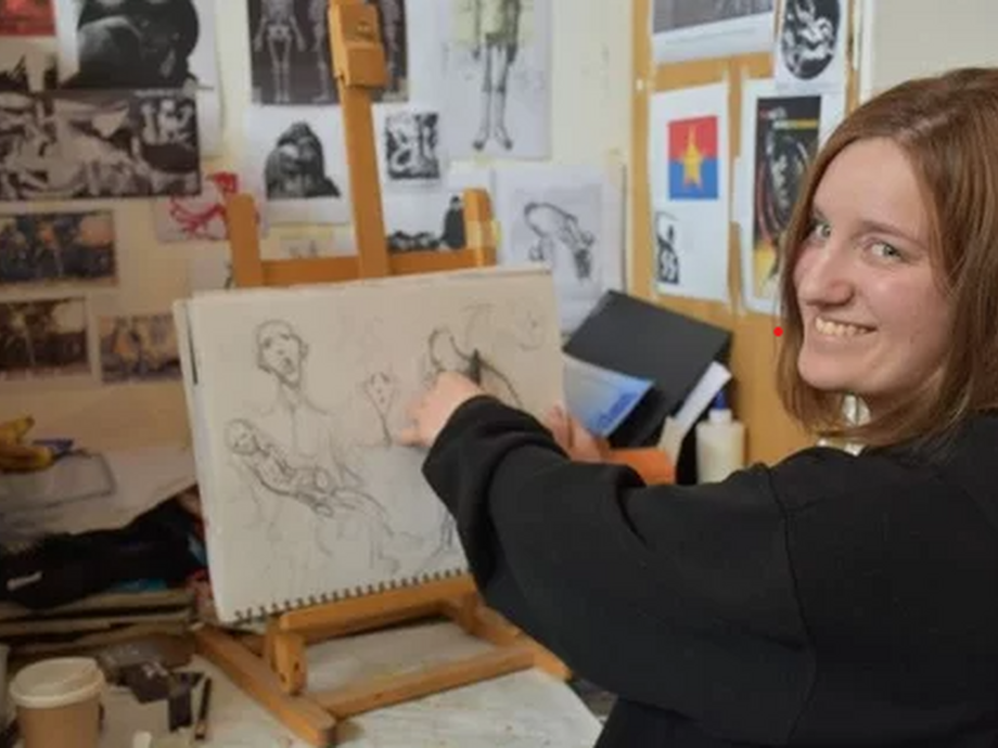 Sitting by an easel surrounded by sketches and creative images