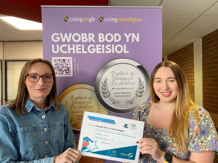 Becky and Ffion from BeAmbitious team holding up award certificate in front of banner