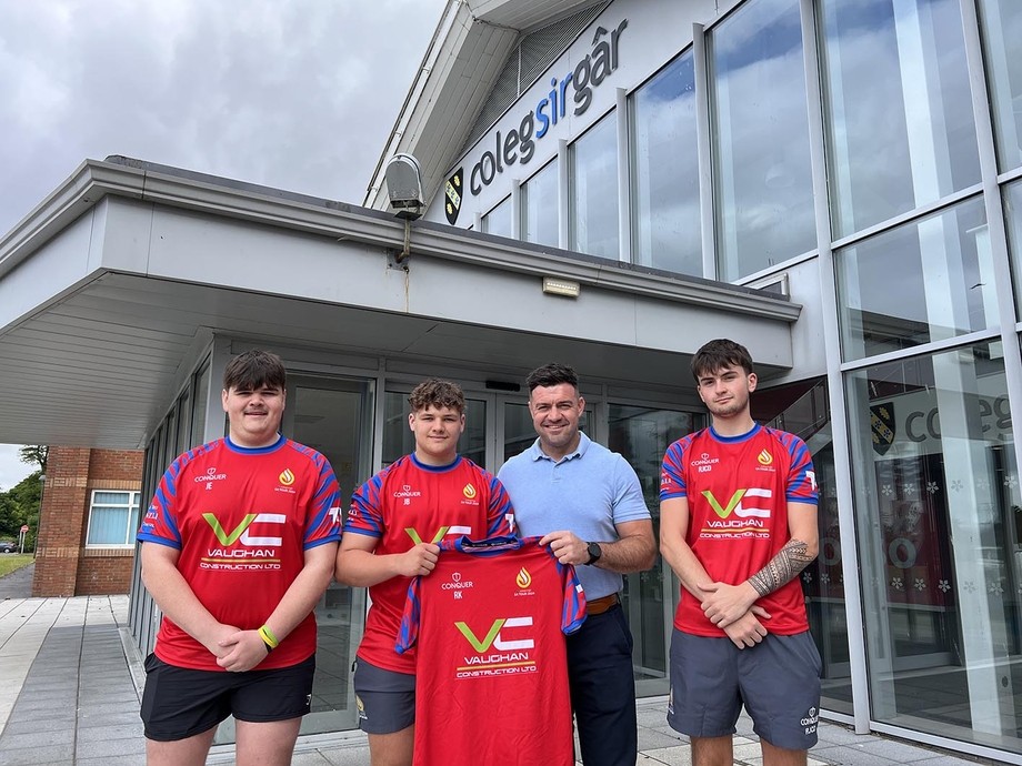 Adam from Vaughan Construction outside the college pictured with some team members wearing red kit and holding up a shirt