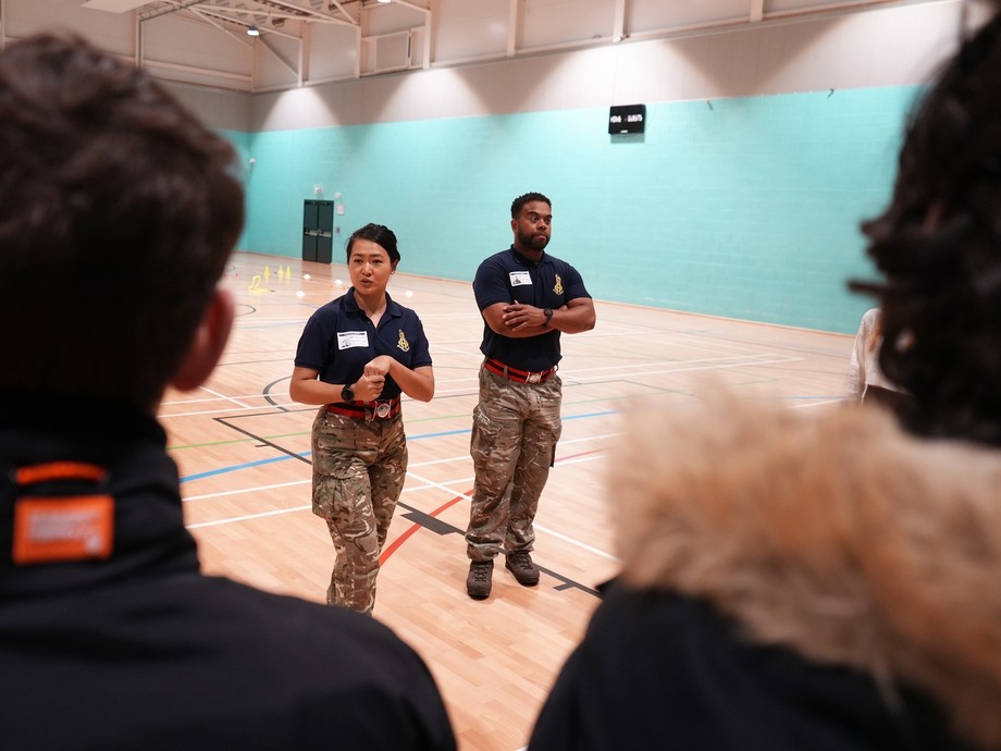 A group of students in a gym, with two British Army members engaging in conversation with students.