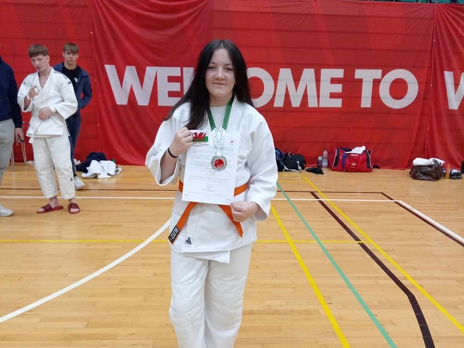 A woman in a white karate uniform proudly holds her certificate, showcasing her achievement in martial arts.