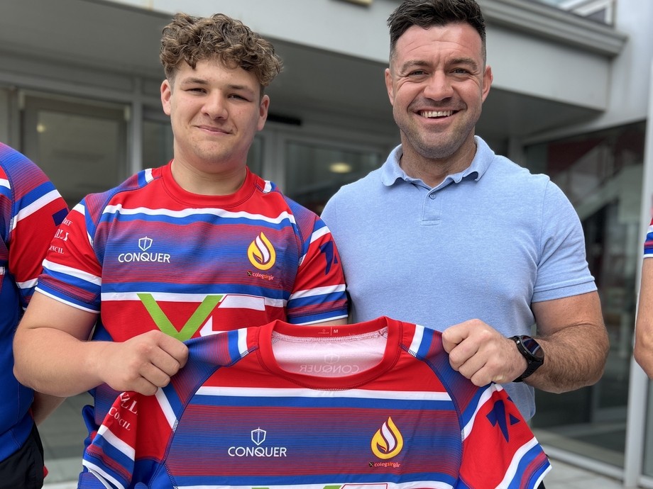 Adam outside the college with a team player holding the blue and red shirt