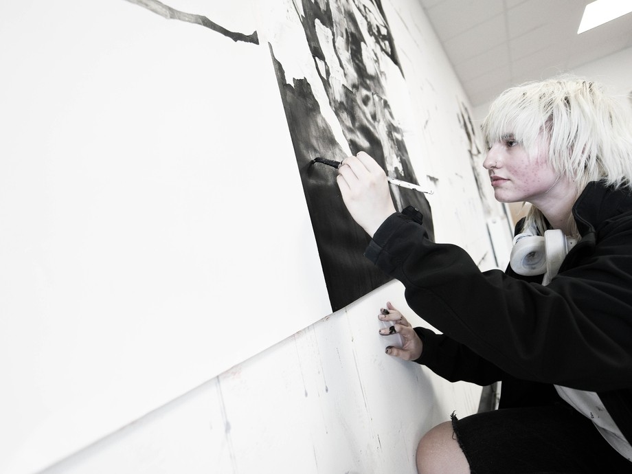 Student white bleached white hair painting on a large canvass with black paint