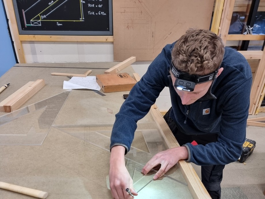A person working on a workbench with a technical drawing in the background