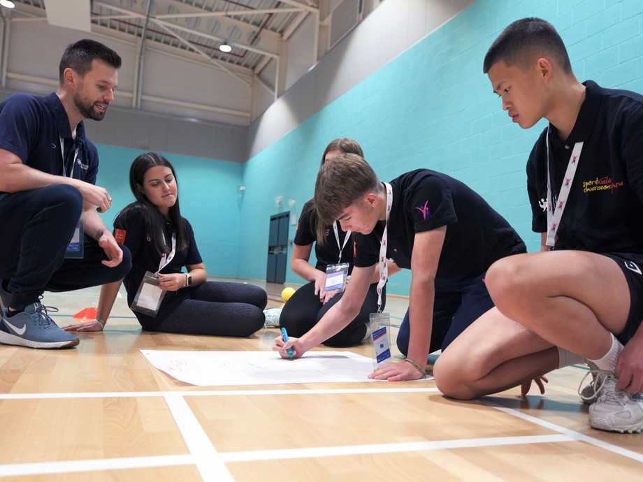 learners sat on the ground in a sports hall completing a mind map during a workshop
