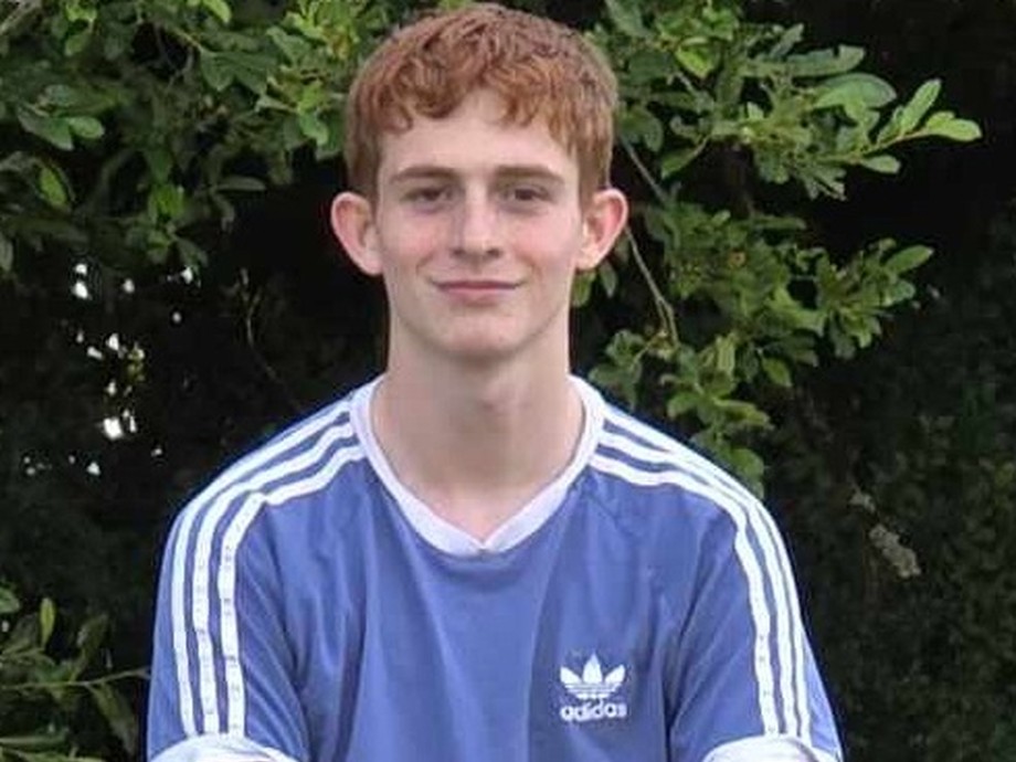 Joseph with greenery behind him sat in a blue short sleeved top looking at the camera