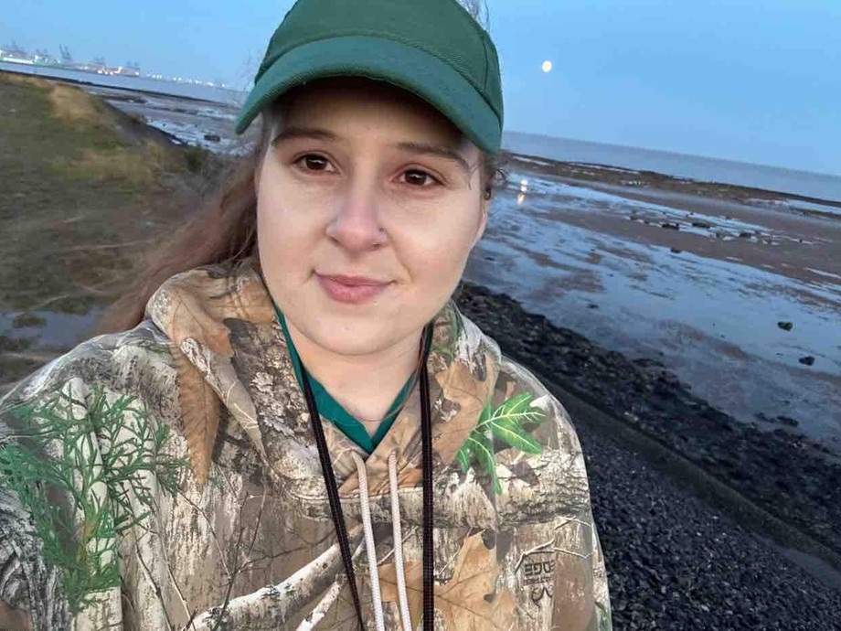 Abbi with a beach behind her wearing a green hat 