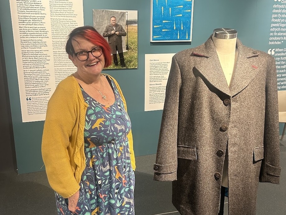 Allison in a mustard cardigan and dress standing next to the coat