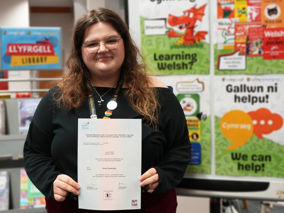 Emily with the library in the background holding her certificate