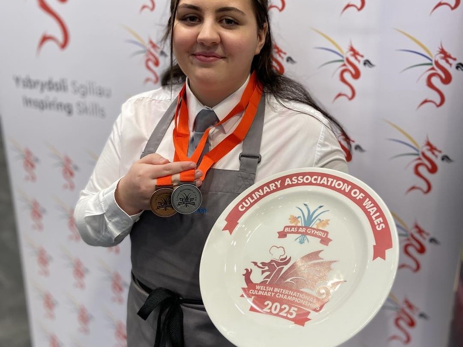 Angharad standing in front of Inspiring Skills branded background holding her medal 