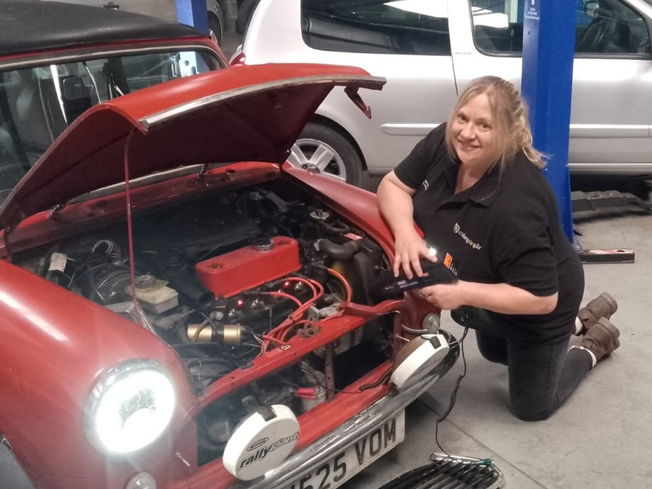 Trudy bending down with a bonnet of a mini up showing the engine