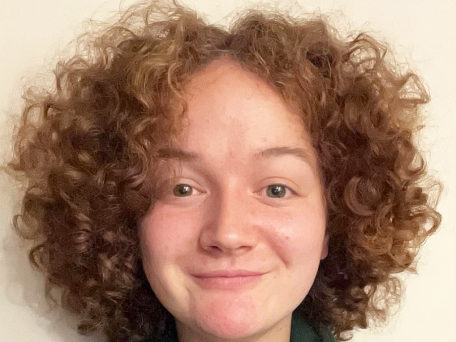 Katie, who has shoulder length curly hair, who is looking at the camera in a green National Botanic Gardens fleece