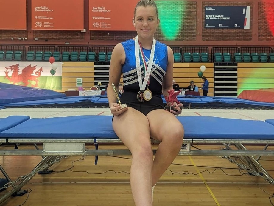 Maddie in professional gym kit with a medal leaning on a trampoline