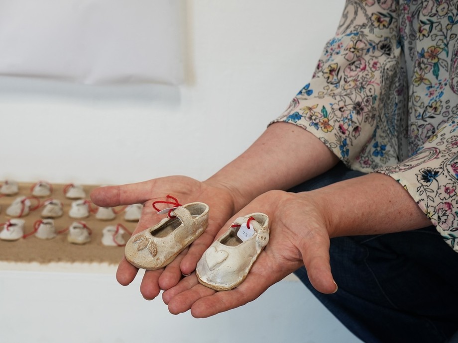 Jenny's hands holding her clay children's shoes with rows of more behind