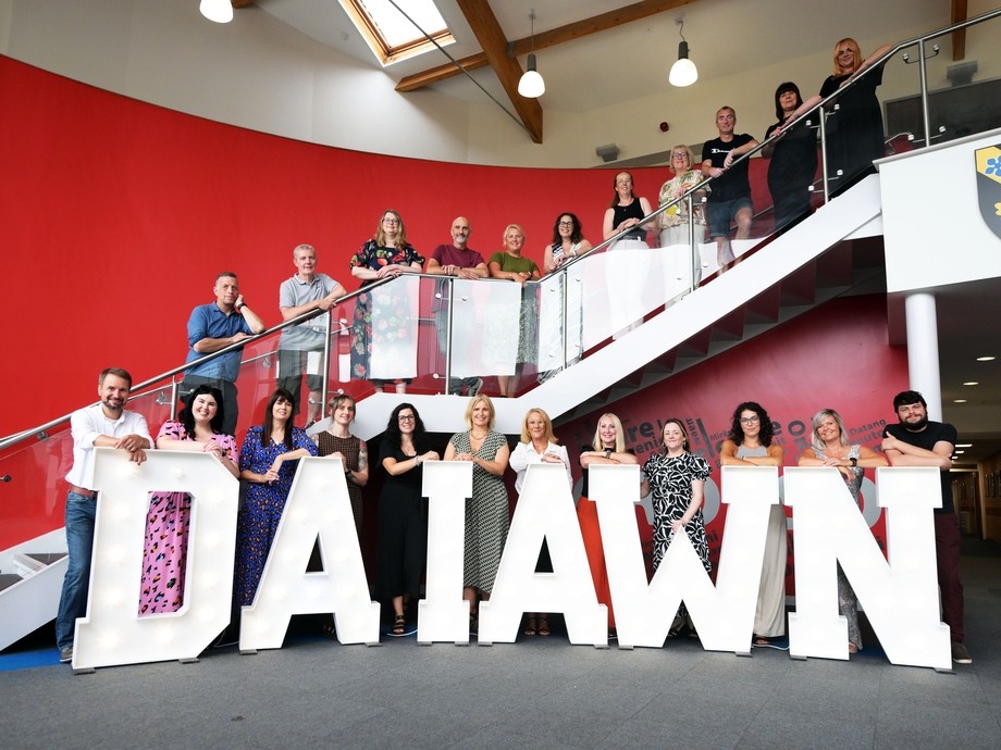 All the A-level tutors lined up on the stairs and balcony with the lighted up words Da Iawn at the bottom 