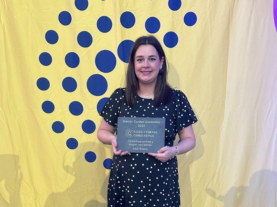 Lisa standing up with the Coleg Cenedlaethol branding in the back holding her award