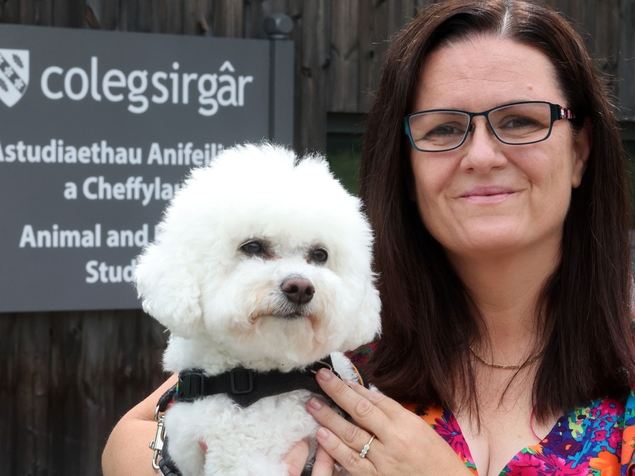 Mandy outside the animal studies centre (with sign) holding her white furred dog Daisy