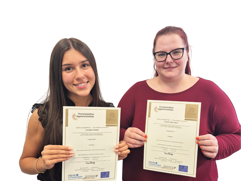 Two young women looking at the camera holding up certificates. 