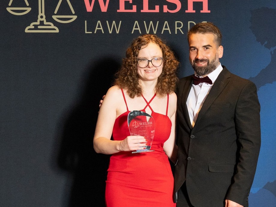 Victoria wearing a red dress with a well dressed man and her award with Welsh Law Awards written in the background