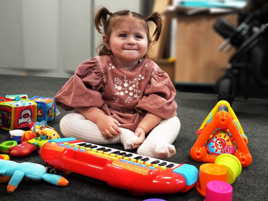 Liwsi playing with some toys smiling sitting on the floor