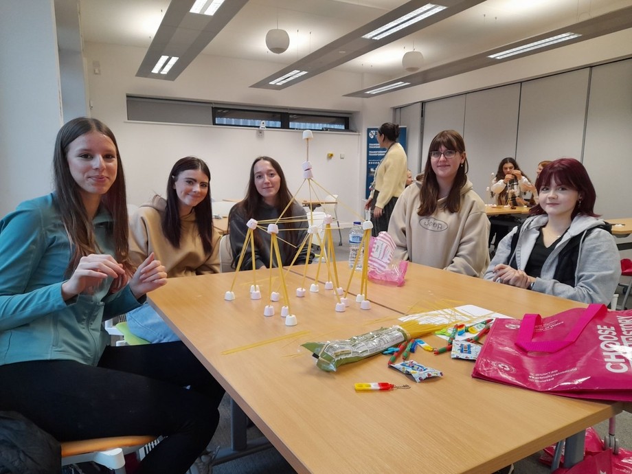 A group of students around a desk building structures from spaghetti and marshmallows