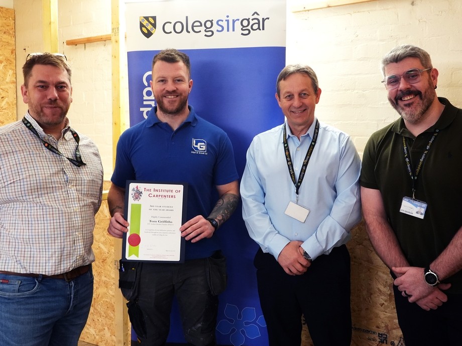 Tom standing with his certificate with tutor Gareth, Wayne and Craig in a carpentry workshop