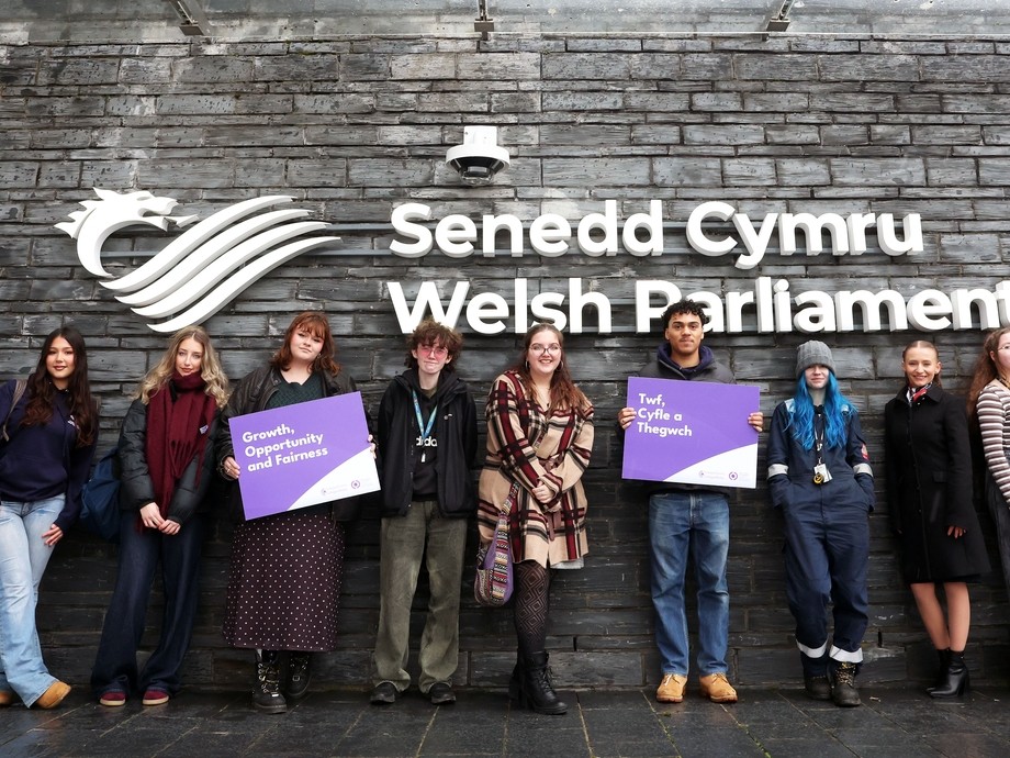 Students outside the Gwersyll yr Urdd building holding up a sign saying, growth, opportunity, fairness