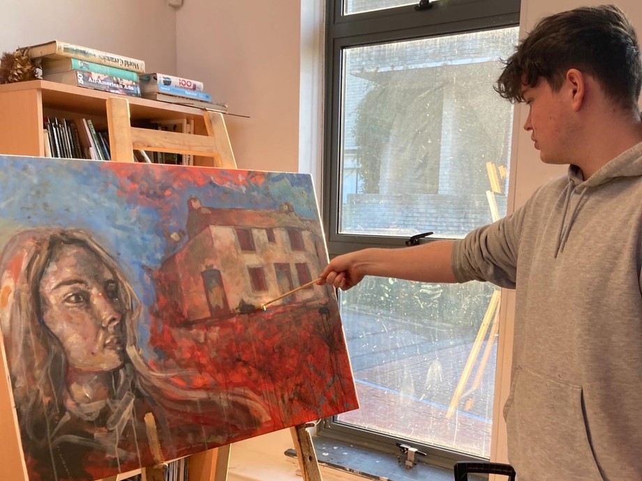 A student painting on an easel it's a face of a woman with a big window behind them