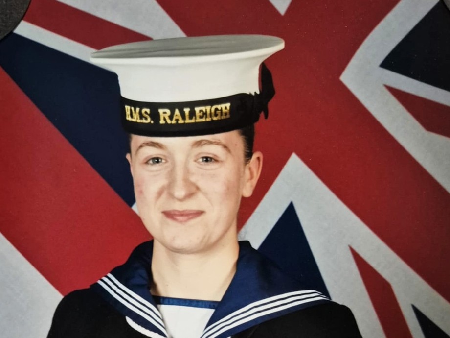 Mia in her Royal Navy uniform in front of the UK flag