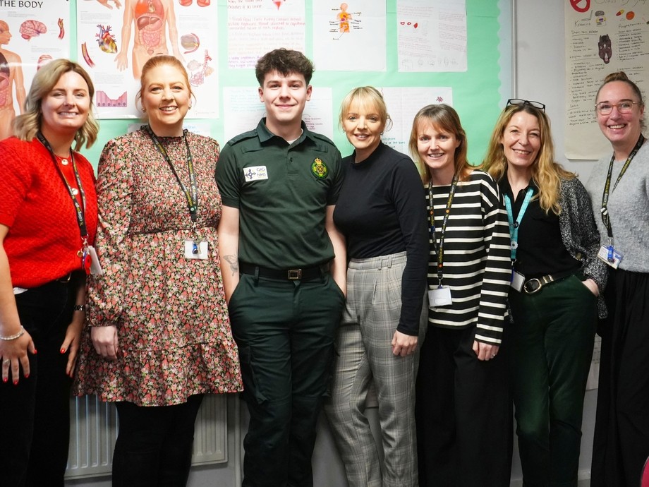 Zach standing in a line with his former health and social care lecturers with a medical background/display board