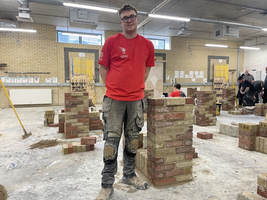 A student in a red t-shirt standing by his finished brickwork construction