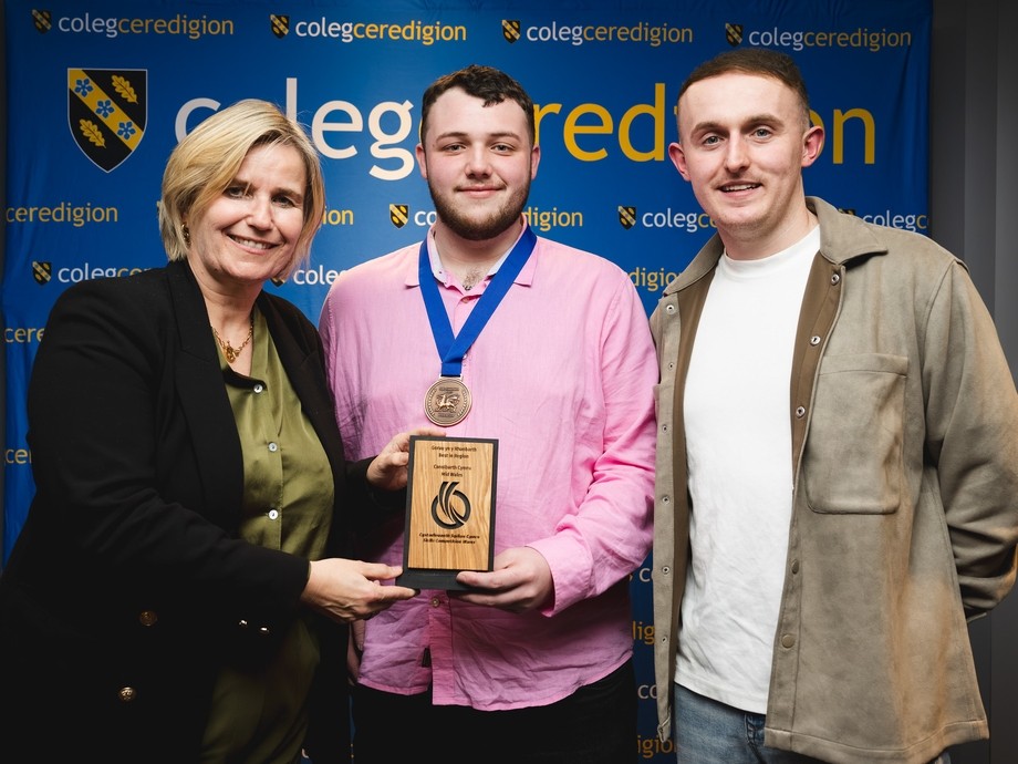Acting principal Vanessa with Glyn and tutor Sam college branding behind Glyn holding skills competition Wales medal
