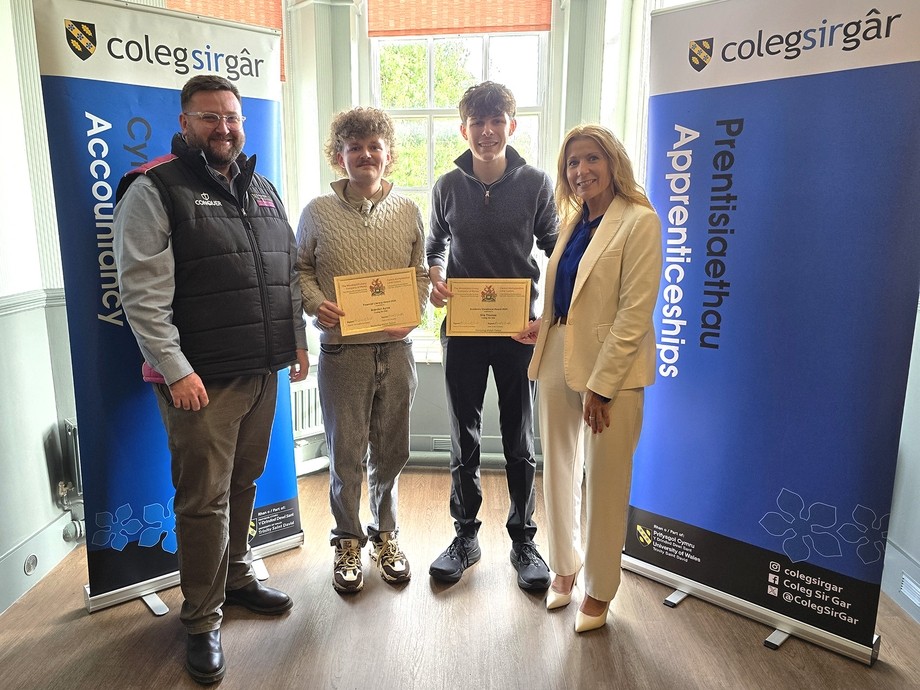 The two apprentices standing with Gareth David and a rep from the Worshipful Livery with two college branded banners on each side (they are holding certificates)