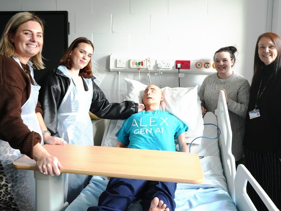 Alex the AI mannequin in a bed with a student and lecturer one side and the other Rebecca and Vicky