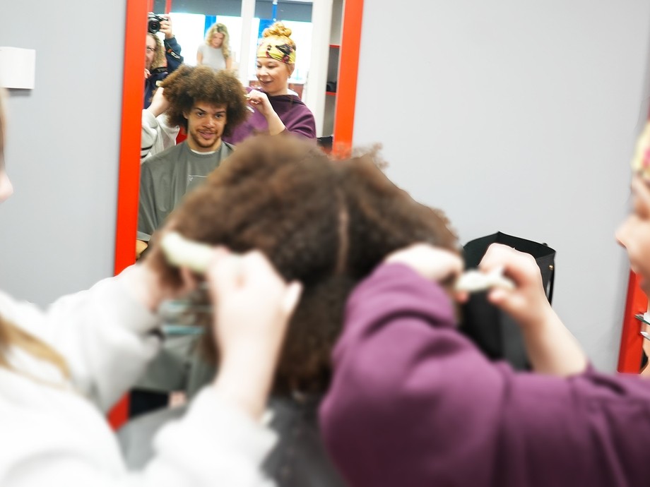 Two hairdressing students working with afro hair on a client who  you can see in a salon mirror