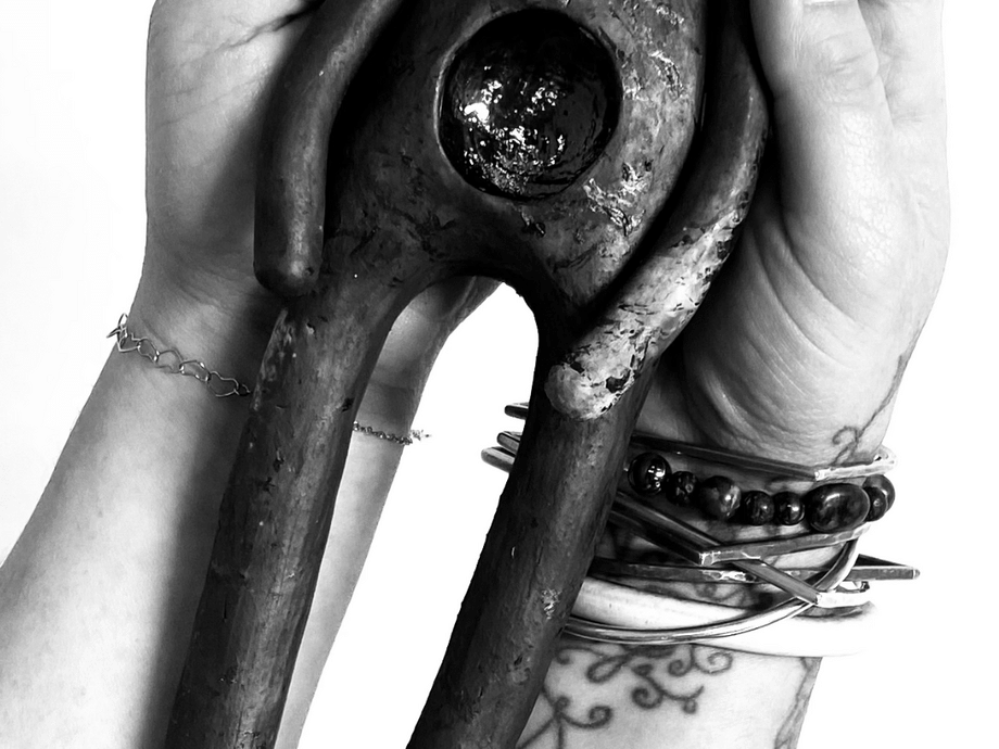 two human hands/arms, one with a tattoo. It's all black and white and they are holding a ceramic piece shaped like a simplified human shape