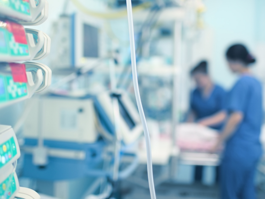 Foreground a medical machine and background blurred nurses seeing to a patient