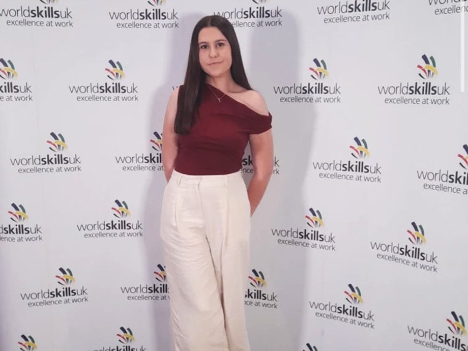 Emily with WorldSkills branding behind her she is dressed smartly