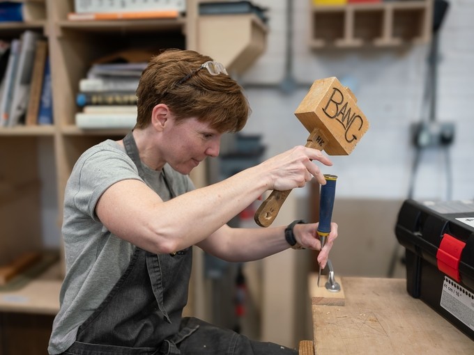 Student in a workshop with a wooden mallet and a chisel.