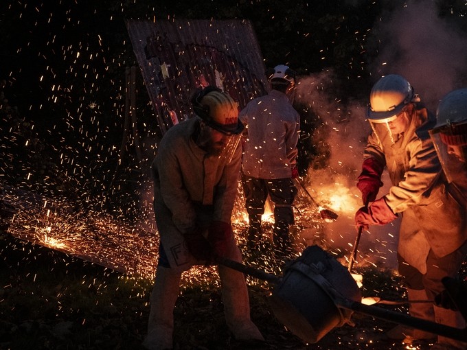 Students in protective clothing working in the metal foundry. The image is dark and highlighted by sparks of metal and fire.