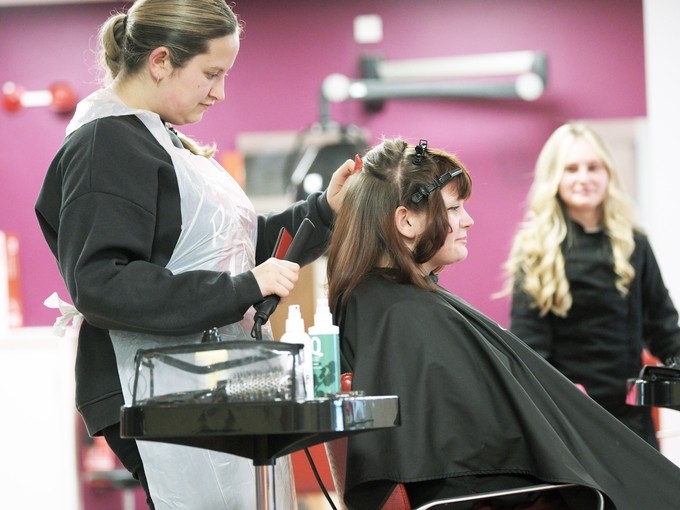 Student in black uniform drying a clients hair in a salon.