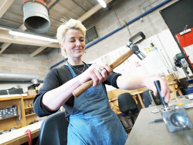 A student hammers some jewellery into shape.