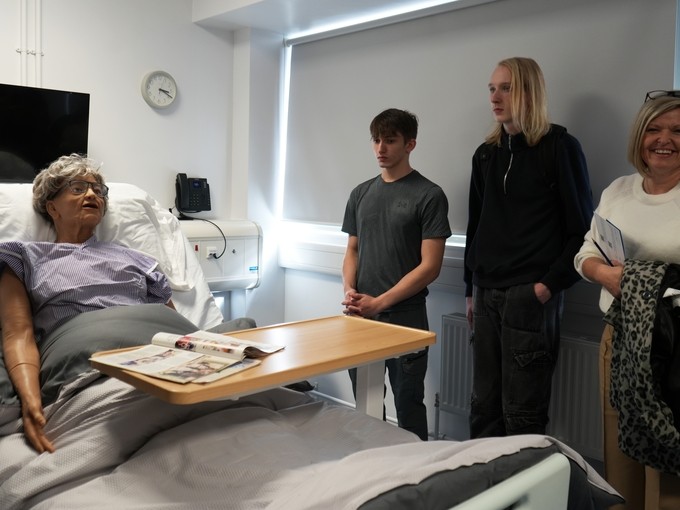 Angharad Mansfield and students in a room with a simulator mannequin sat up in bed