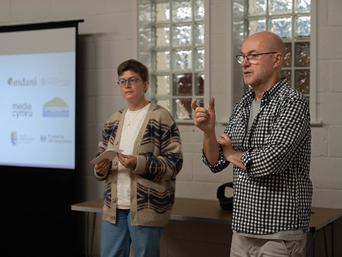 Amy Daniel and Huw Penallt Jones standing by a projector screen taking to a group