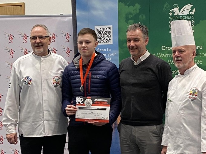 Standing with medal around neck in chef's whites with the other chefs/judges