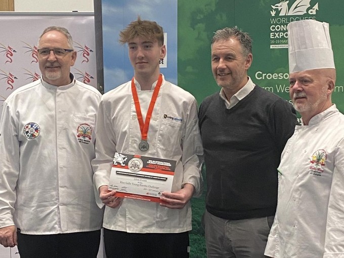 Standing with medal around neck in chef's whites with the other chefs/judges