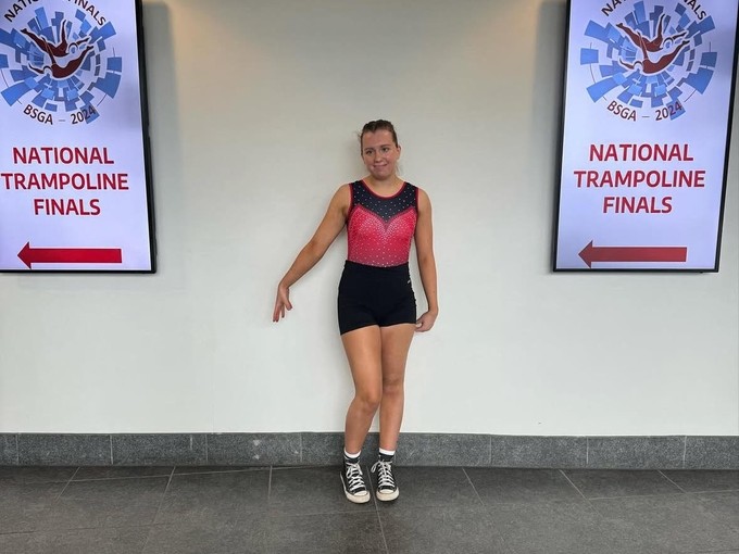 Maddie in front of signs saying National Trampoline Final