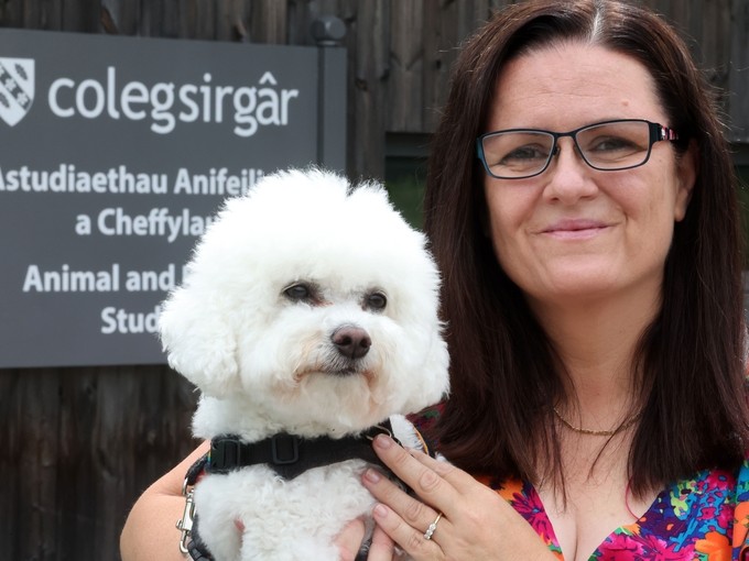 Mandy outside the animal studies centre (with sign) holding her white furred dog Daisy