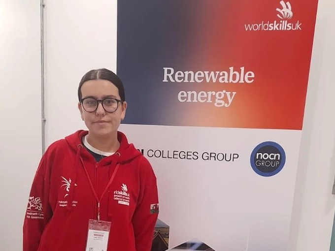 Emily looking at the camera with a skills branded top and a branded roller banner behind her saying renewable energy